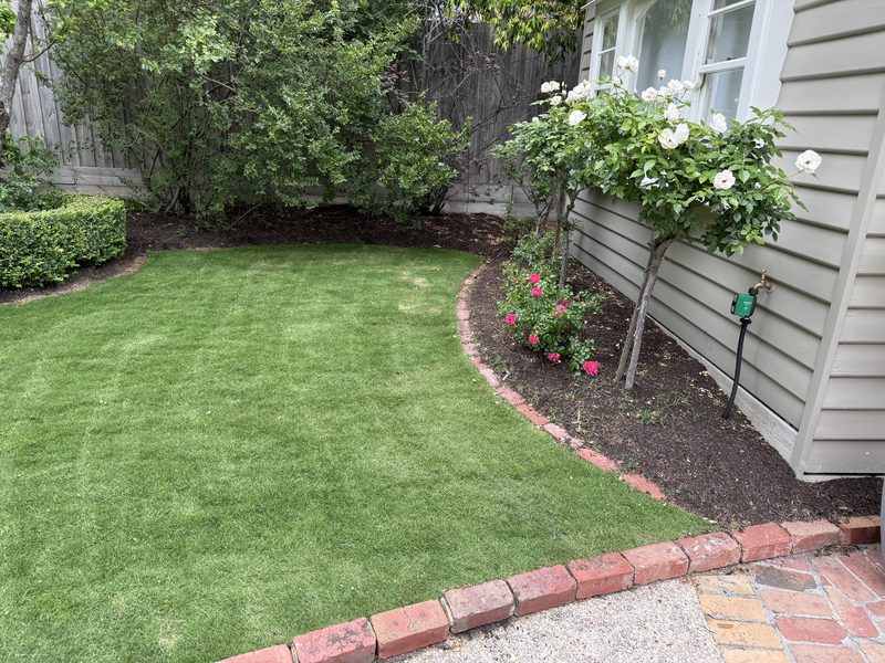 A manicured lawn with brick edging beside a weatherboard cottage